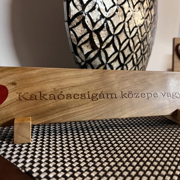 Egyedi kialakítású fa asztaldísz, melynek közepén vagy feliratában kakaóscsigám motívum található, továbbá epoxy piros szívvel berakva.